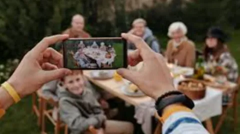 Person holding phone taking a photo of family around outdoor dining table.e