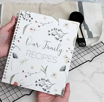 hands holding a spiral bound cookbook that has Our Family recipes on the front