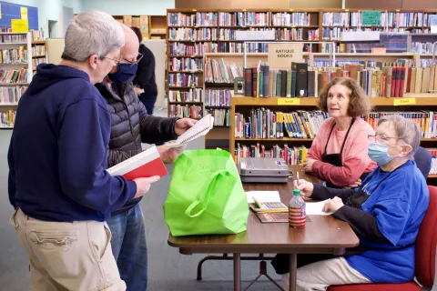Friends volunteers around a table at a used book sale.