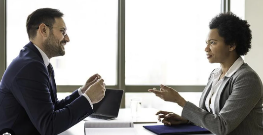 Man and woman across desk from each other conducting an interview.