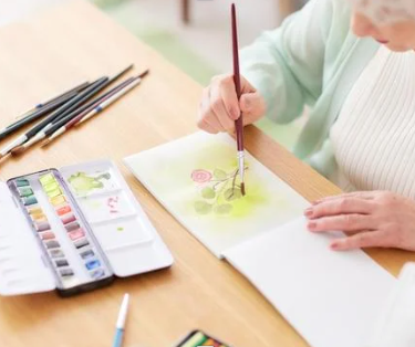 lady in green sweater painting flowers on a canvas